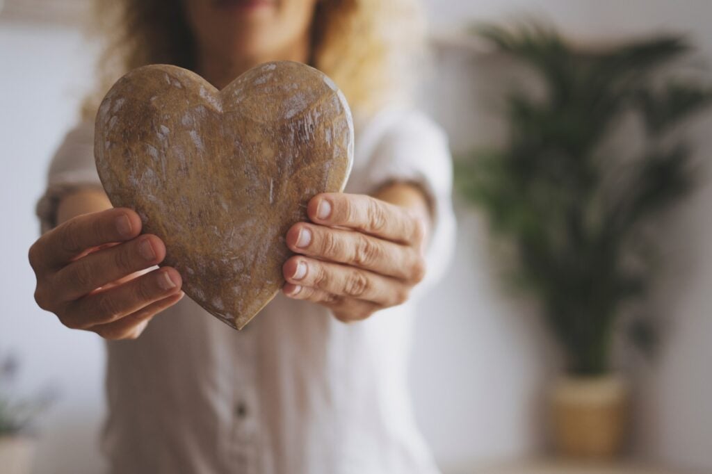 Close up of wooden heart decoration. Woman hold wood decor for love symbol at home.